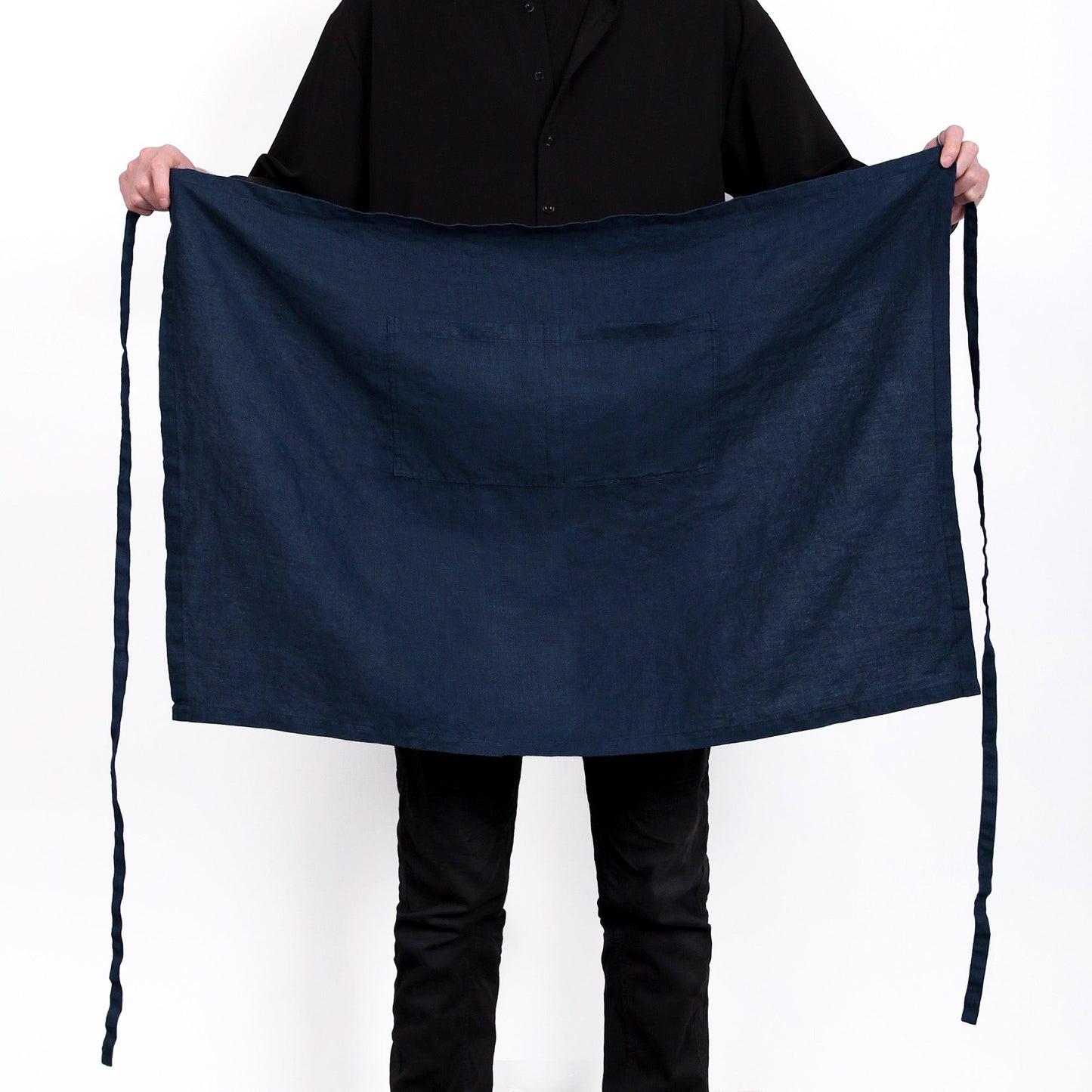 A person holding up a large dark navy blue apron with a front pocket, shown against a plain white background.