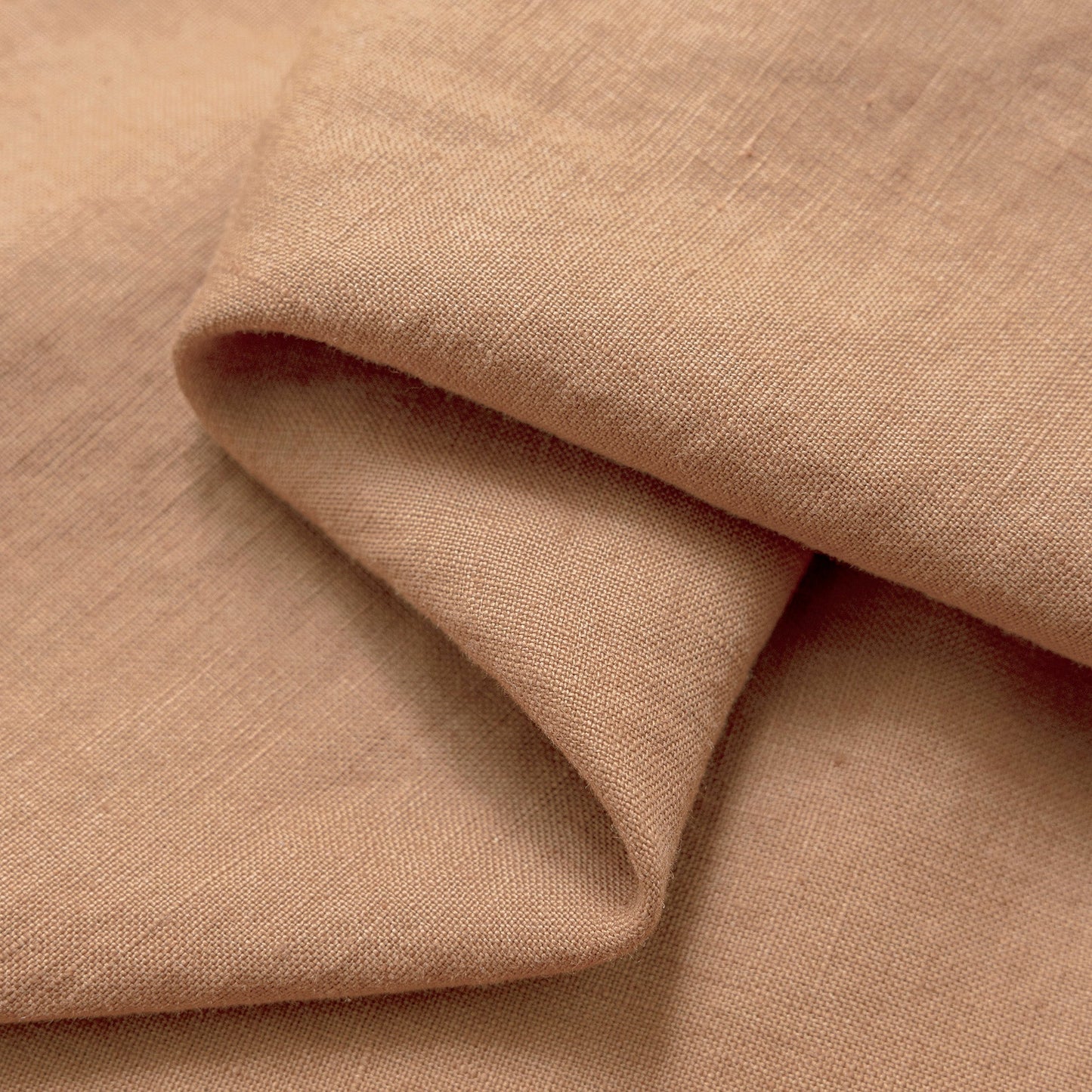 A close-up of draped fabric in a warm dusty tan or blush-beige color, showing the woven texture and soft folds.