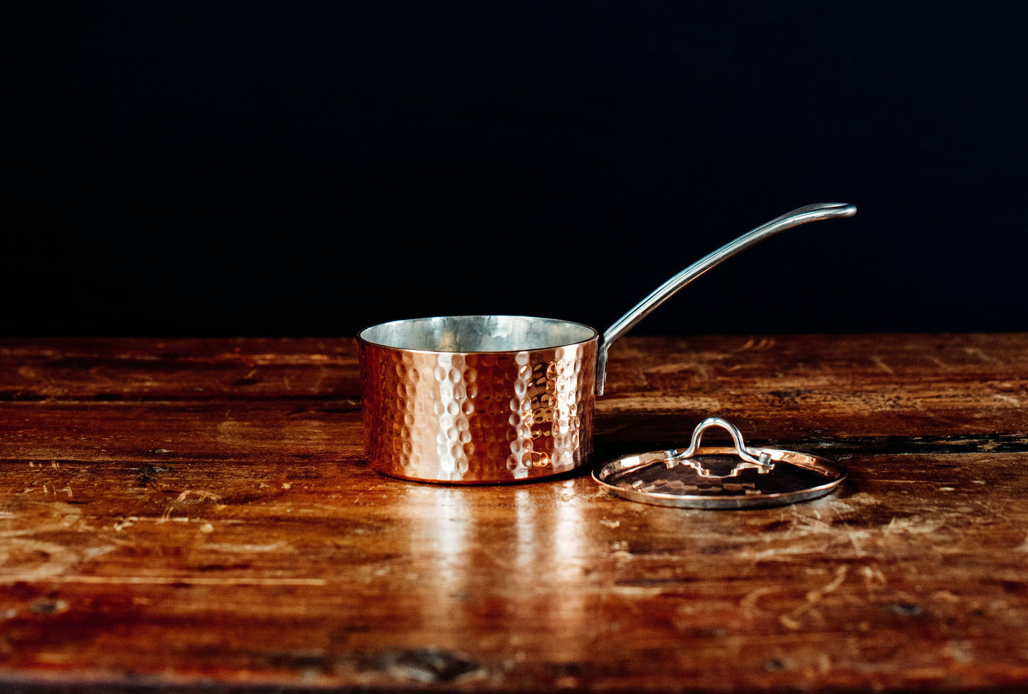 Copper saucepan butter pot with an open lid on a wooden surface
