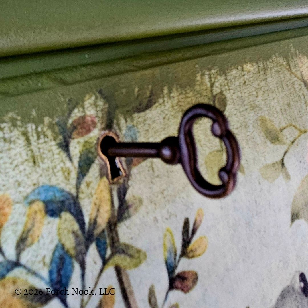 Close-up of vintage style key hardware on botanical decoupage surface of painted secretary desk