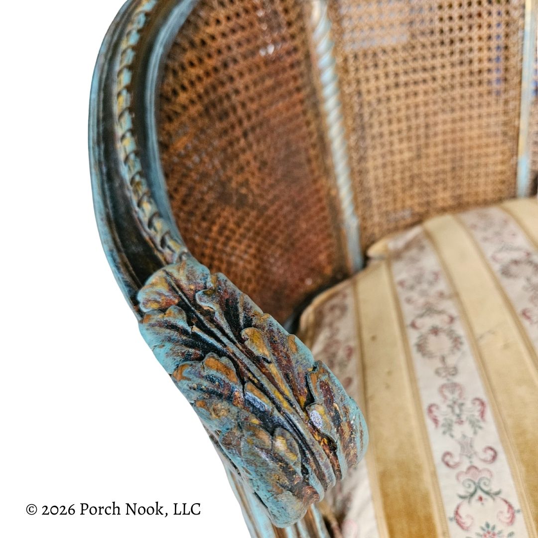 Close-up of an ornate hand carved chair with a caned backrest and decorative armrests on a white background.