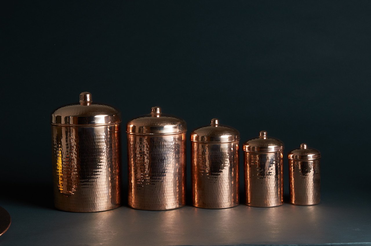Set of five copper canisters of varying sizes on a dark background