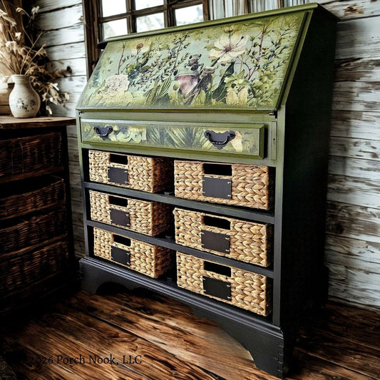 Vintage secretary desk with hand-painted green and black ombre finish, fold-down front panel with botanical frog decoupage, and rattan basket storage styled in a rustic interior