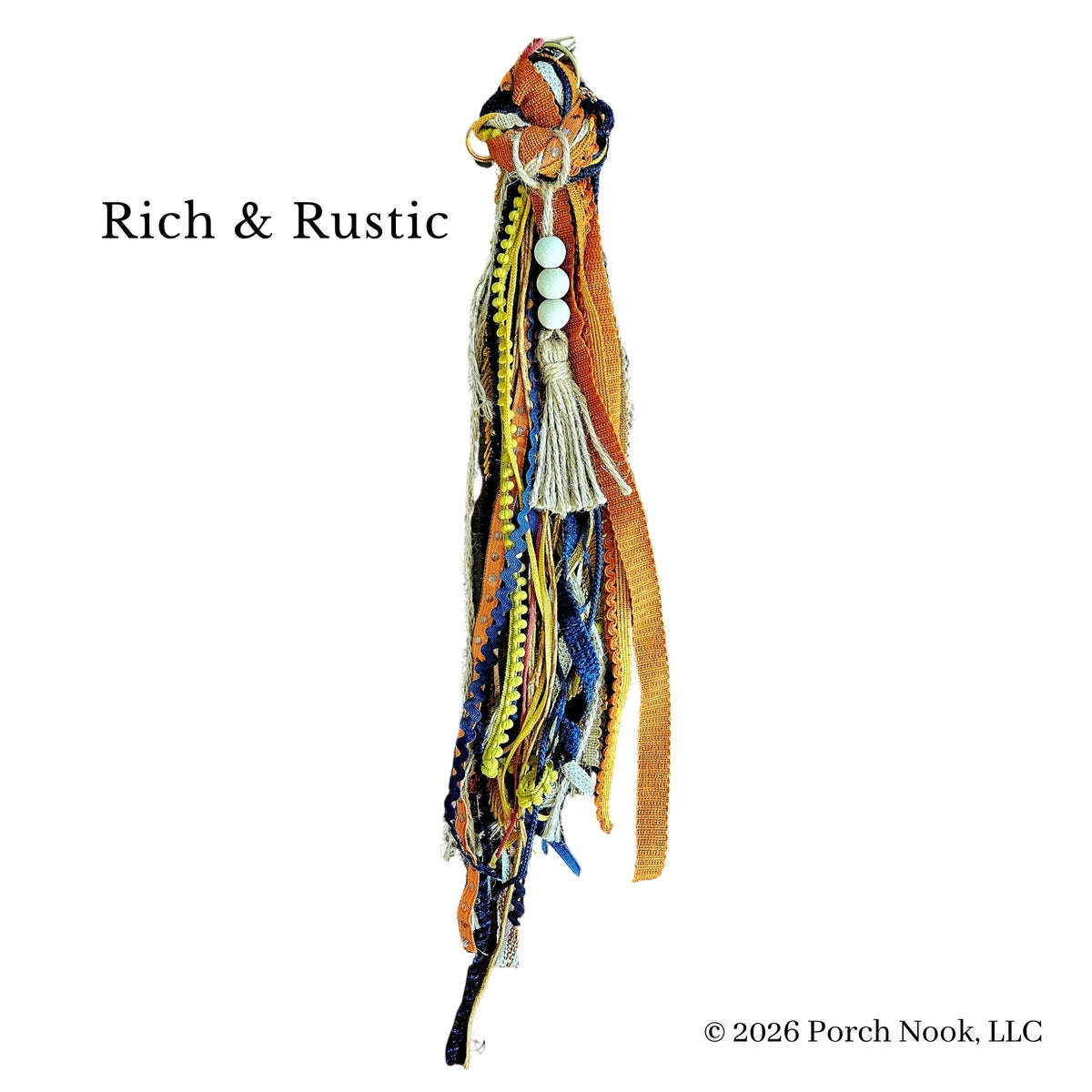 A bohemian-style tassel charm or decorative hanging piece with multiple woven and braided fabric strips in orange, yellow, blue, cream, and brown, accented by white beads and a cream tassel. The text 'Rich & Rustic' appears on the left, and a copyright notice for 'Porch Nook, LLC' appears on the bottom right, all on a plain white background.