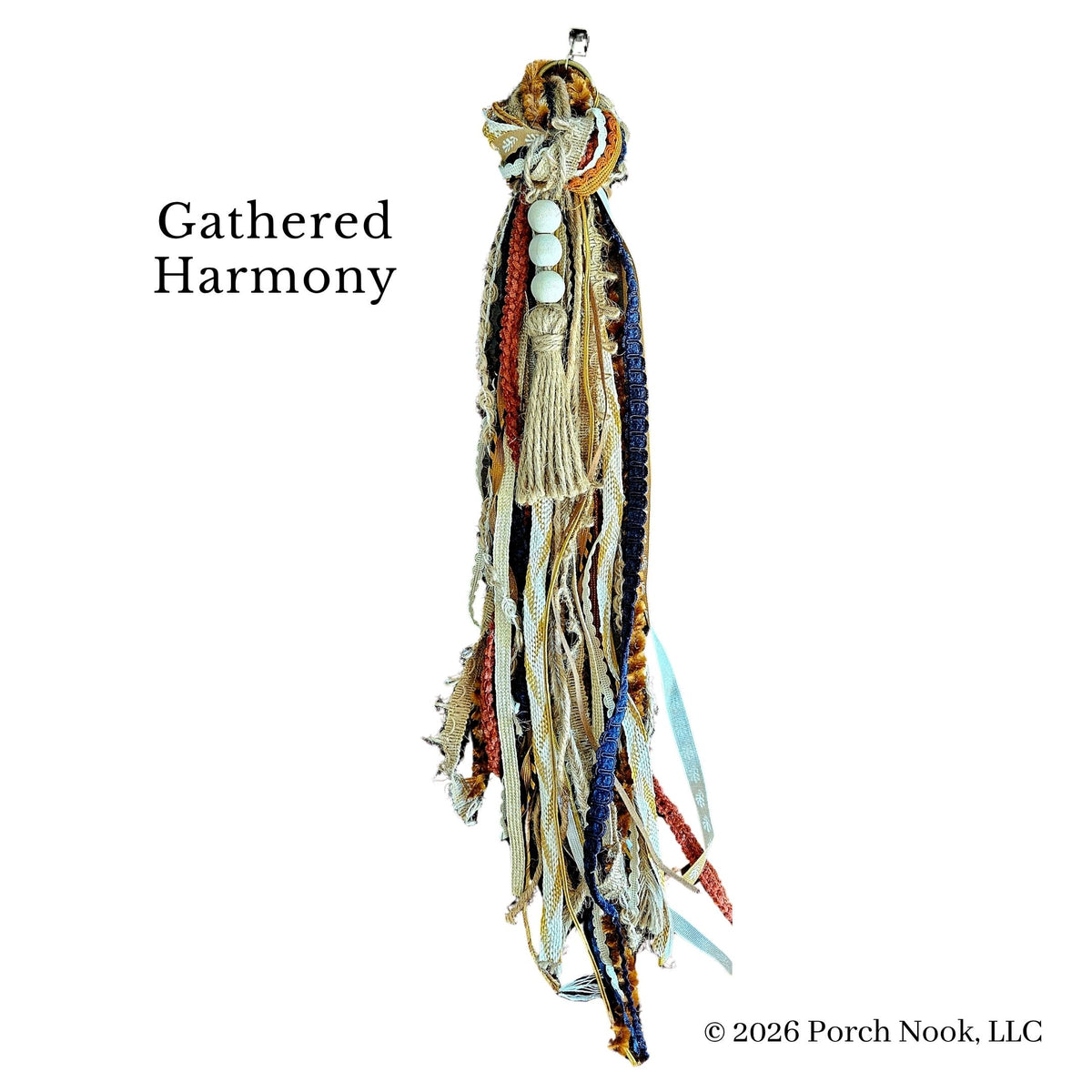 A handmade beaded fringe tassel or wall hanging labeled 'Gathered Harmony' on a plain white background. The piece features multiple strands of cream, tan, brown, blue, and red beads with white circular beads near the top.