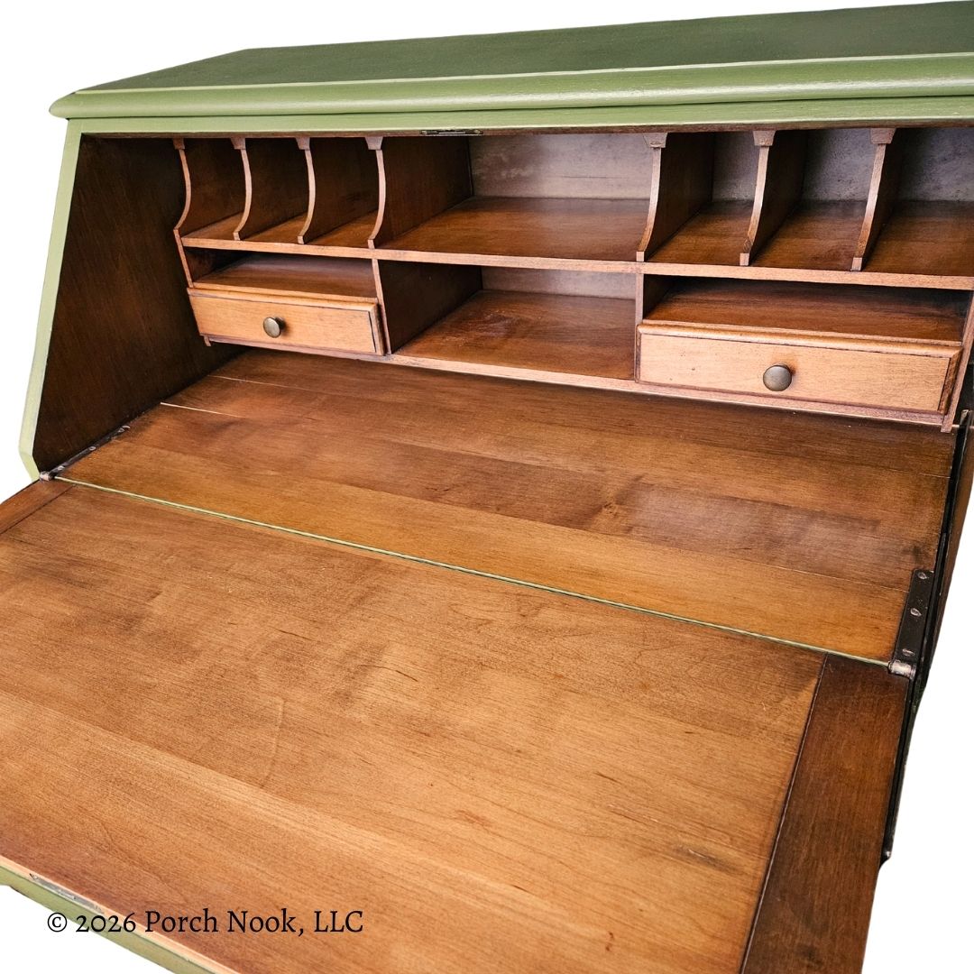 Interior of vintage secretary desk with fold-down writing surface open, showing original wood interior, pigeonholes, and small storage drawers