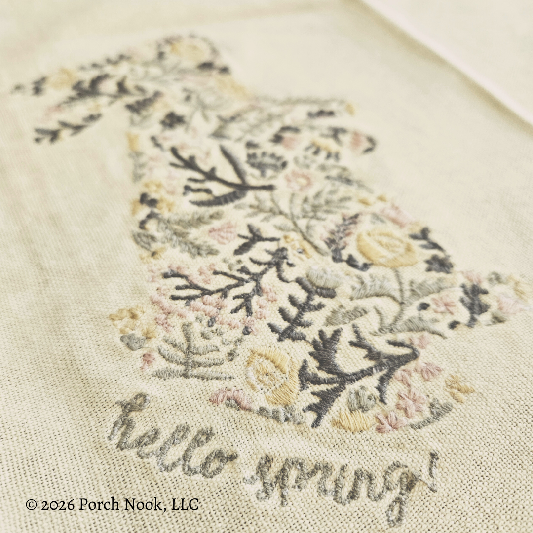 Embroidered design on fabric with floral pattern and 'hello spring!' text, featuring Porch Nook, LLC branding.