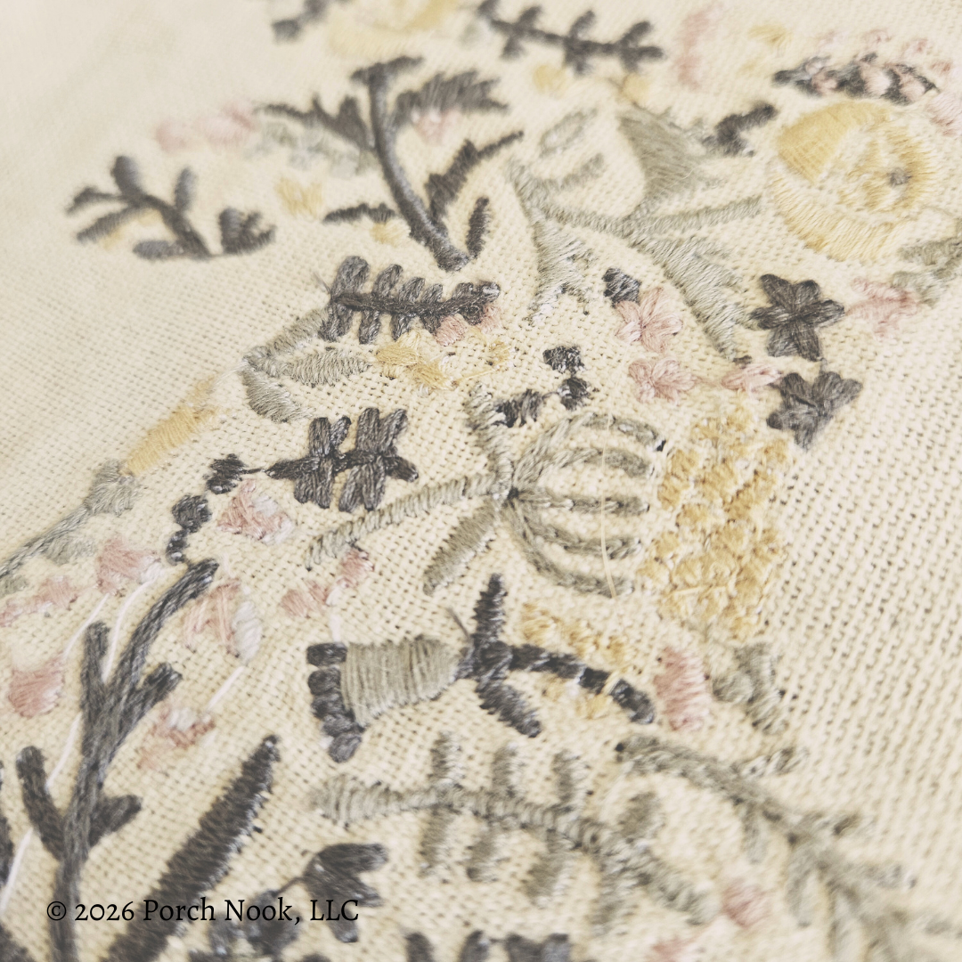 Close-up of embroidered fabric with floral patterns and text '© 2026 Porch Nook, LLC'.