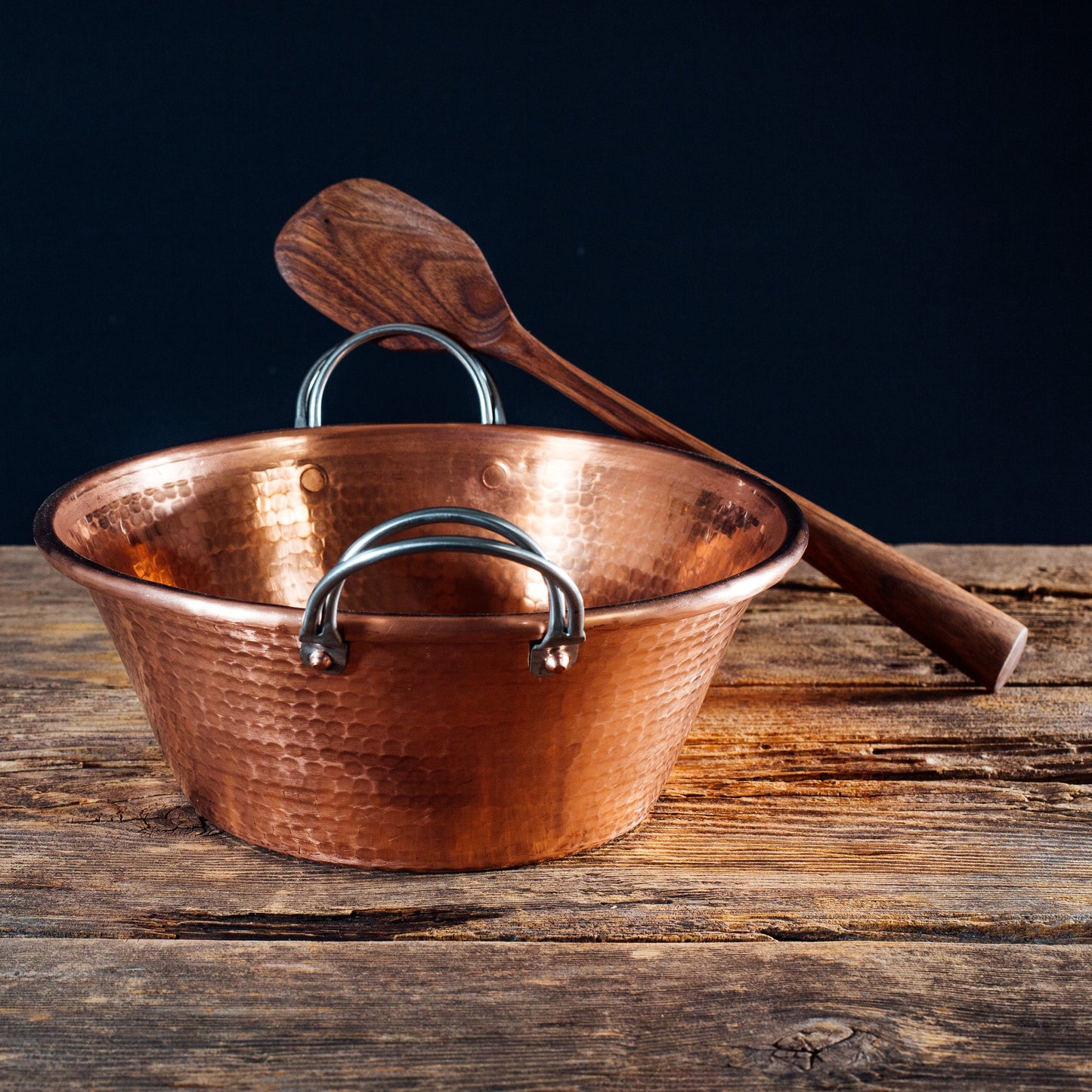Copper pot with wooden spoon on a wooden surface