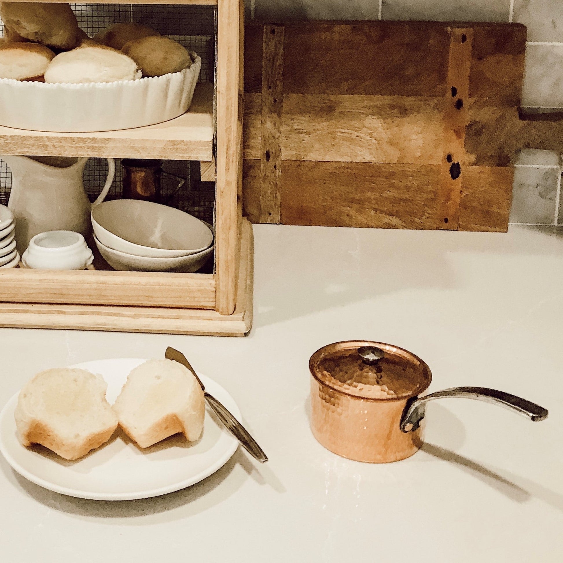 Kitchen counter with copper pot, plate of bread, and wooden cutting board.