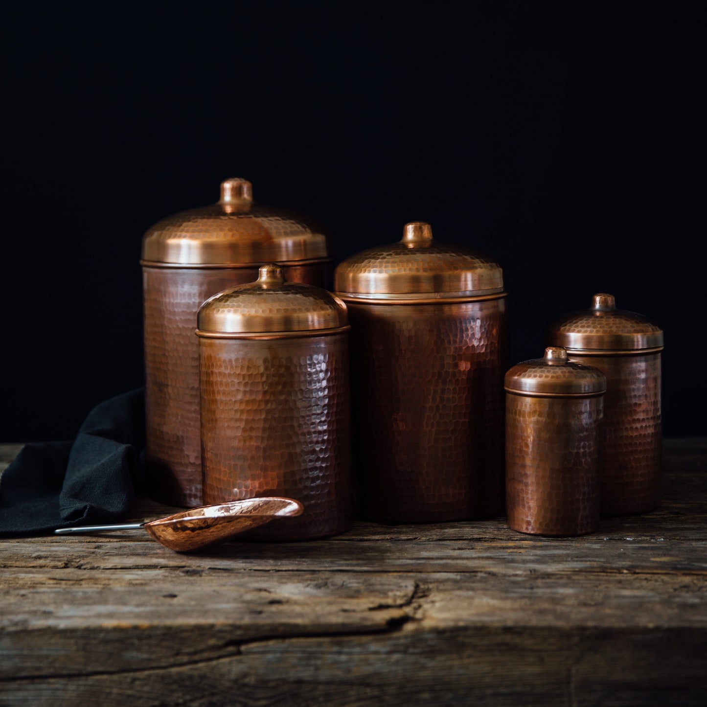 Set of copper canisters on a wooden surface with a dark background