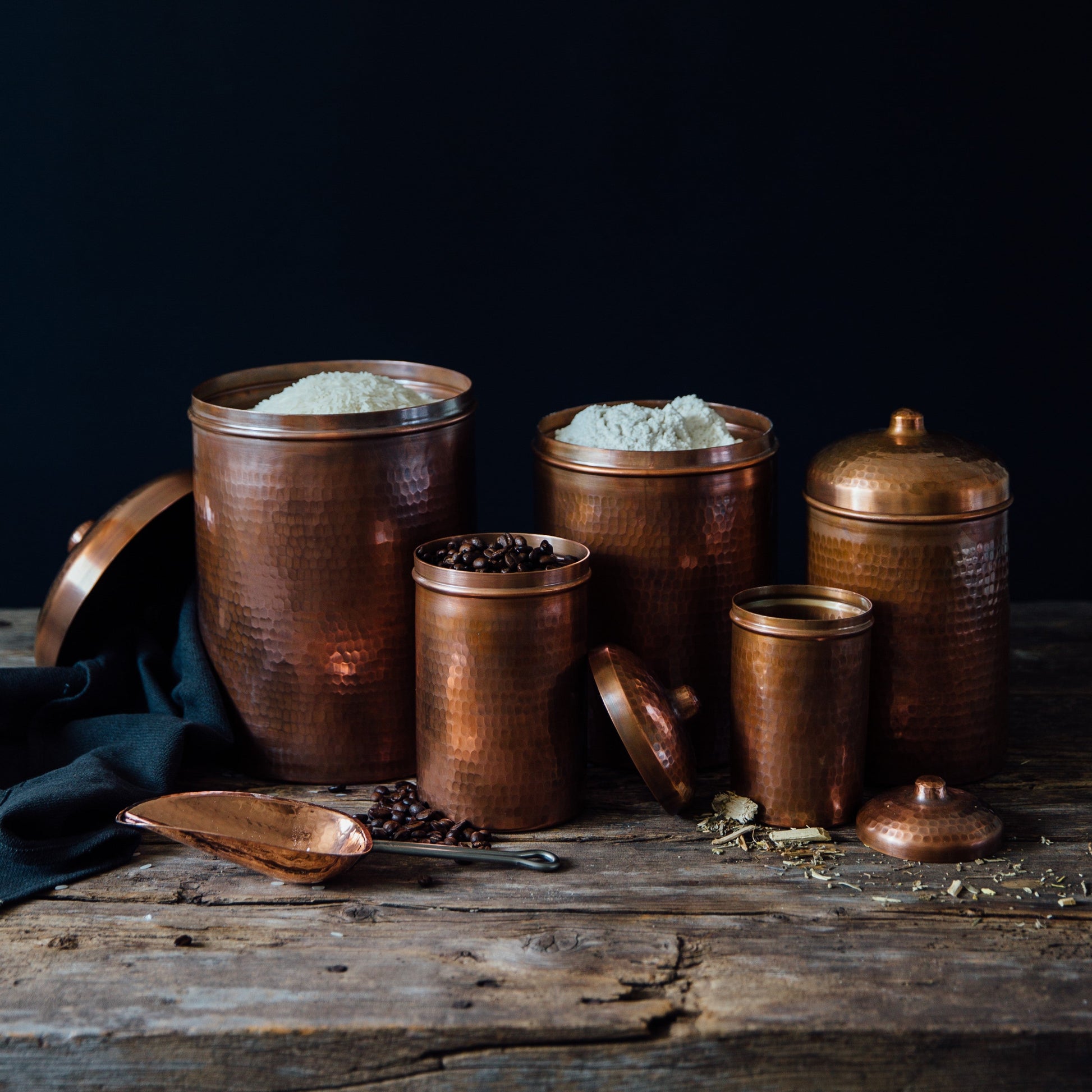 Set of copper containers with lids on a wooden surface against a dark background