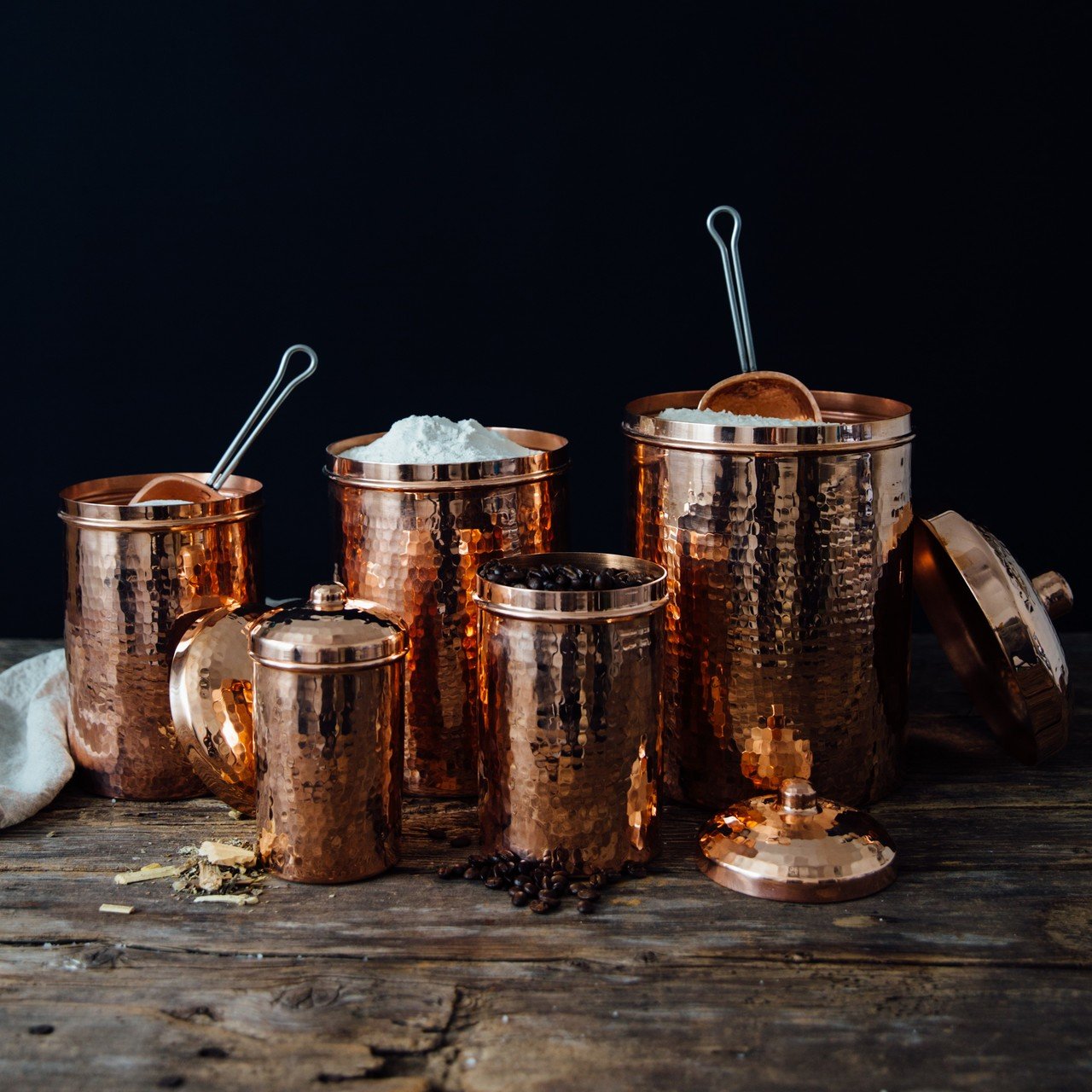 Set of copper canisters with lids on a wooden surface against a dark background
