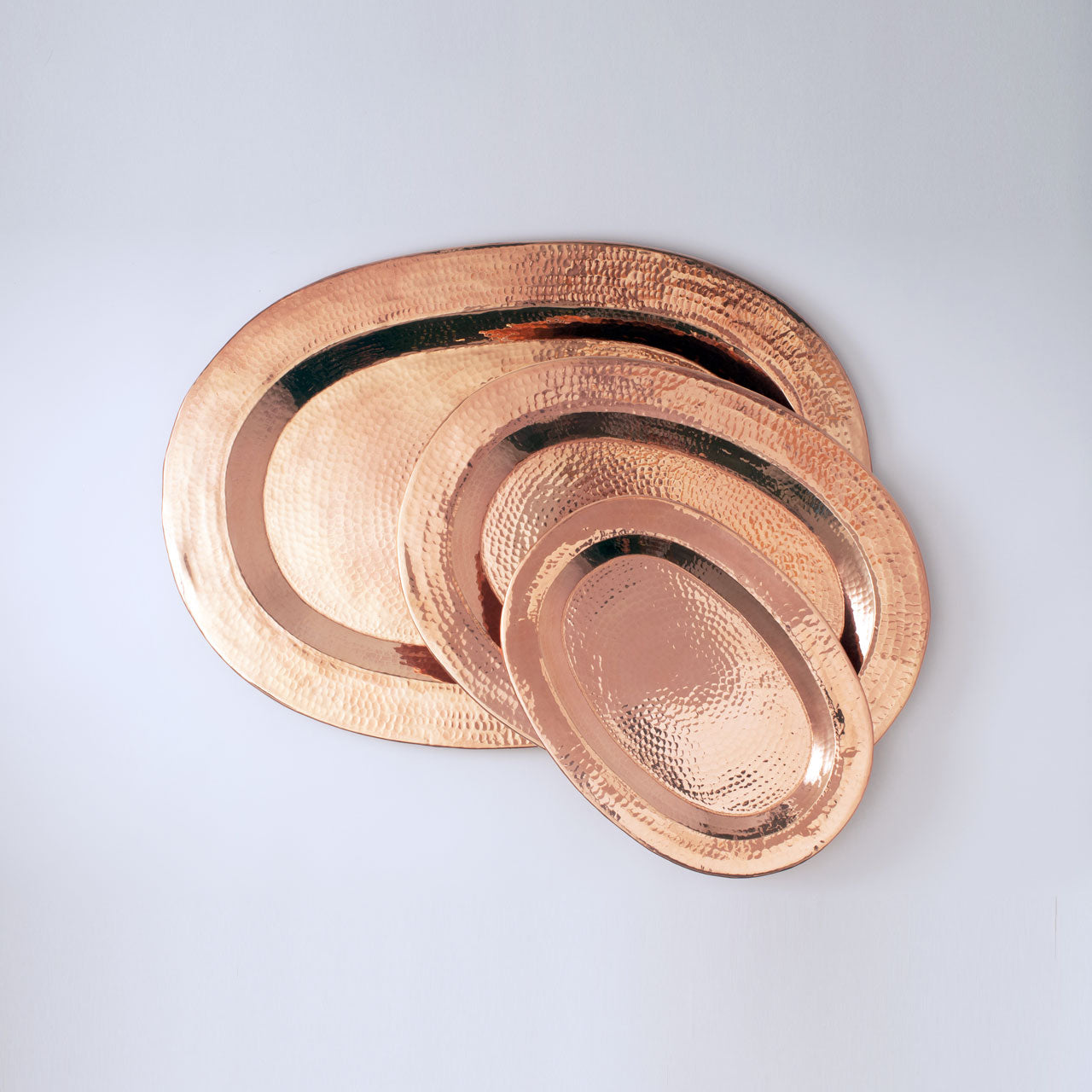 Set of three copper oval trays on a light gray background
