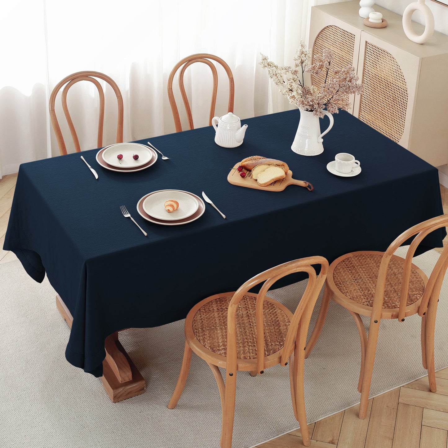 Dining table set with a navy blue tablecloth, plates, cutlery, and a teapot.