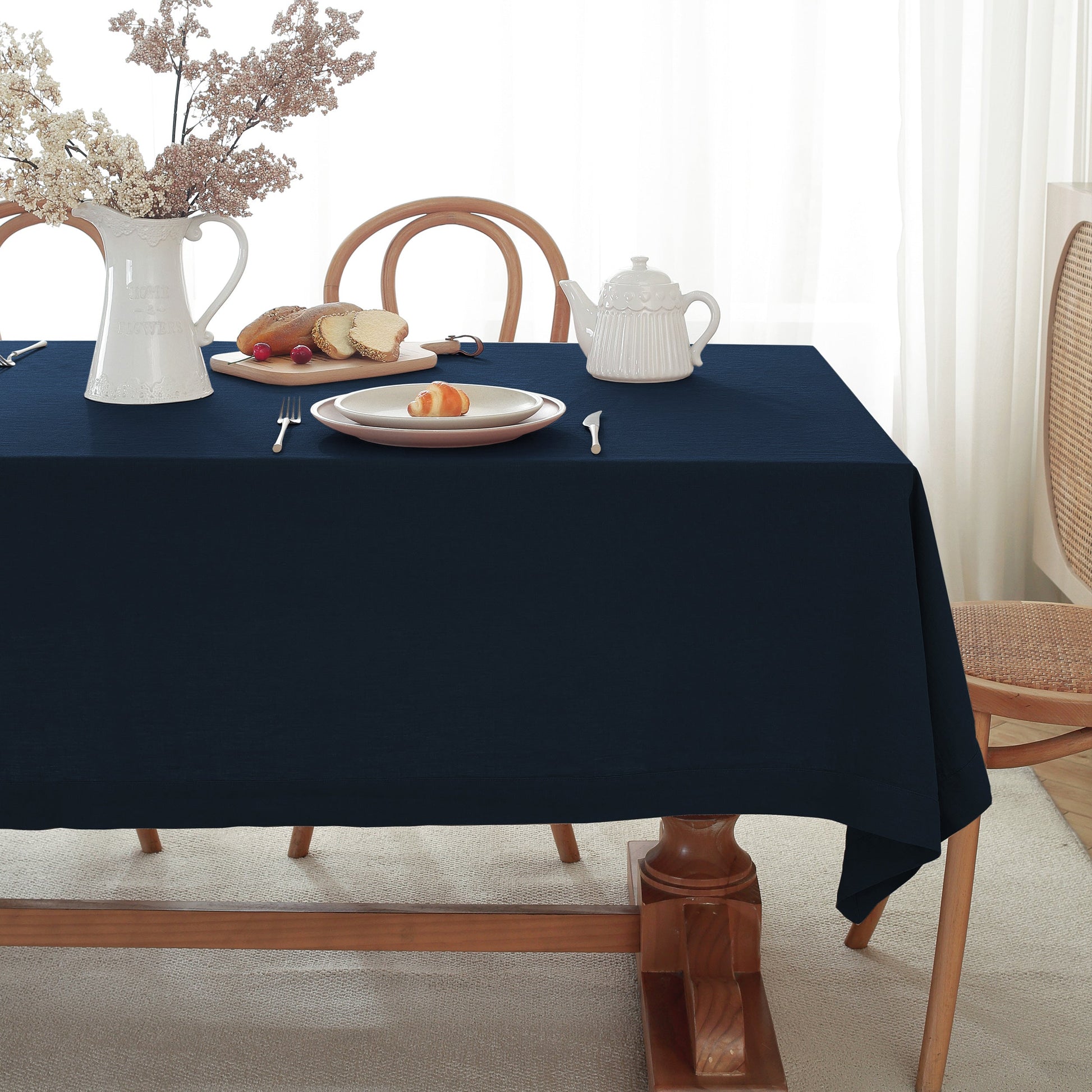 Navy blue tablecloth on a wooden table with white teapot, plate, and pitcher.