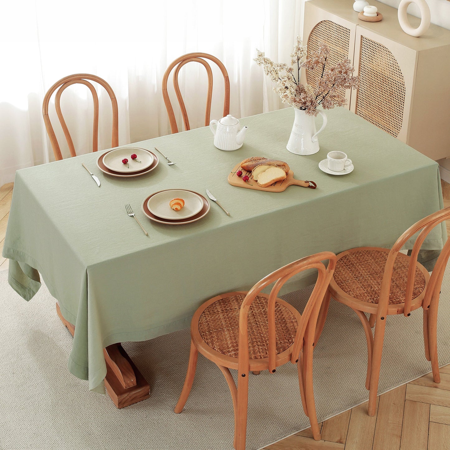 Dining table set with a green tablecloth, plates, cutlery, and a teapot.