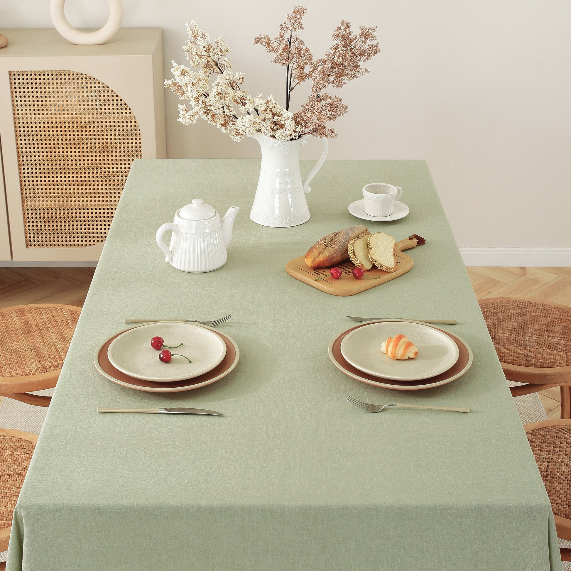 Dining table set with plates, teapot, and bread on a green tablecloth.