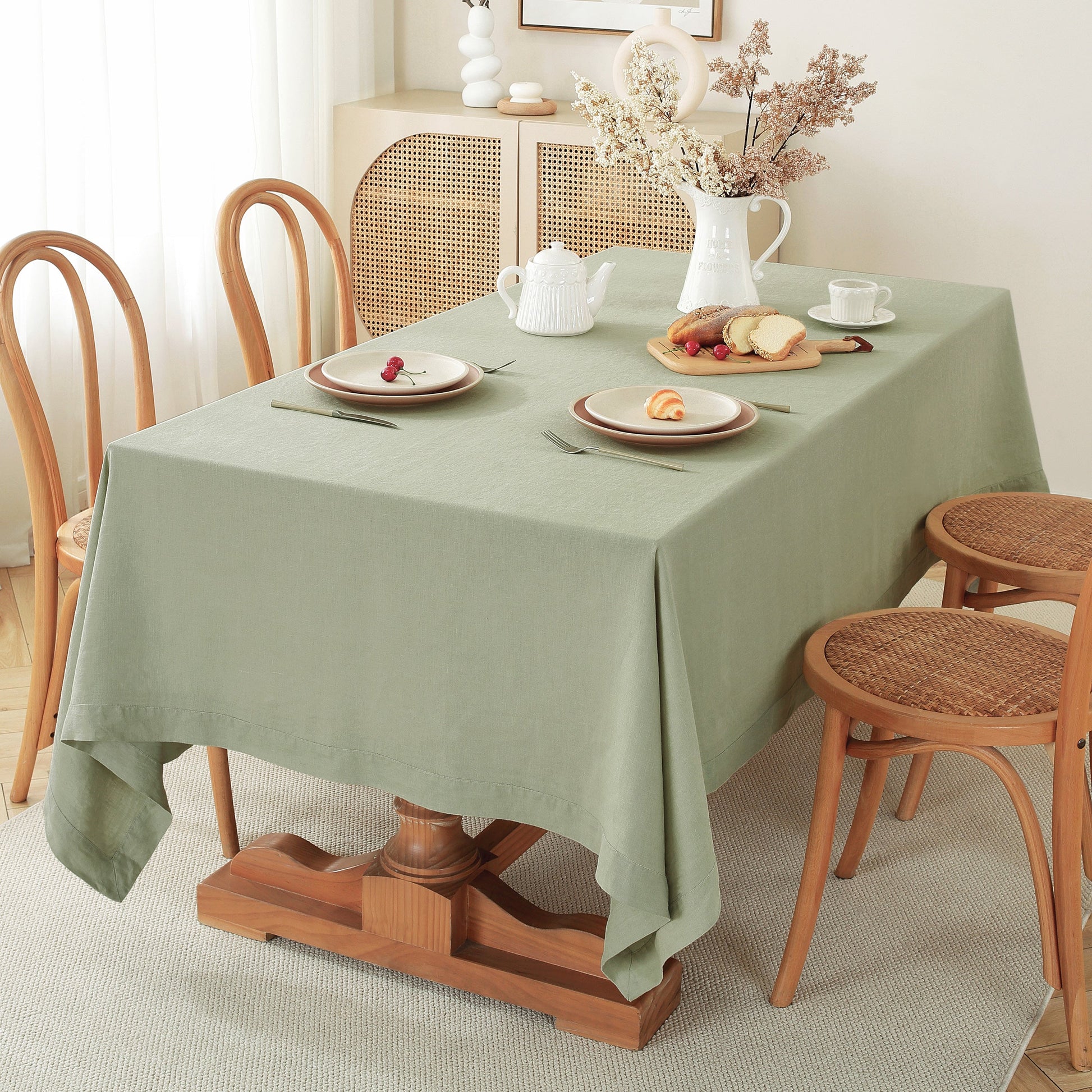 Dining table set with a green tablecloth, plates, and cutlery in a cozy room.