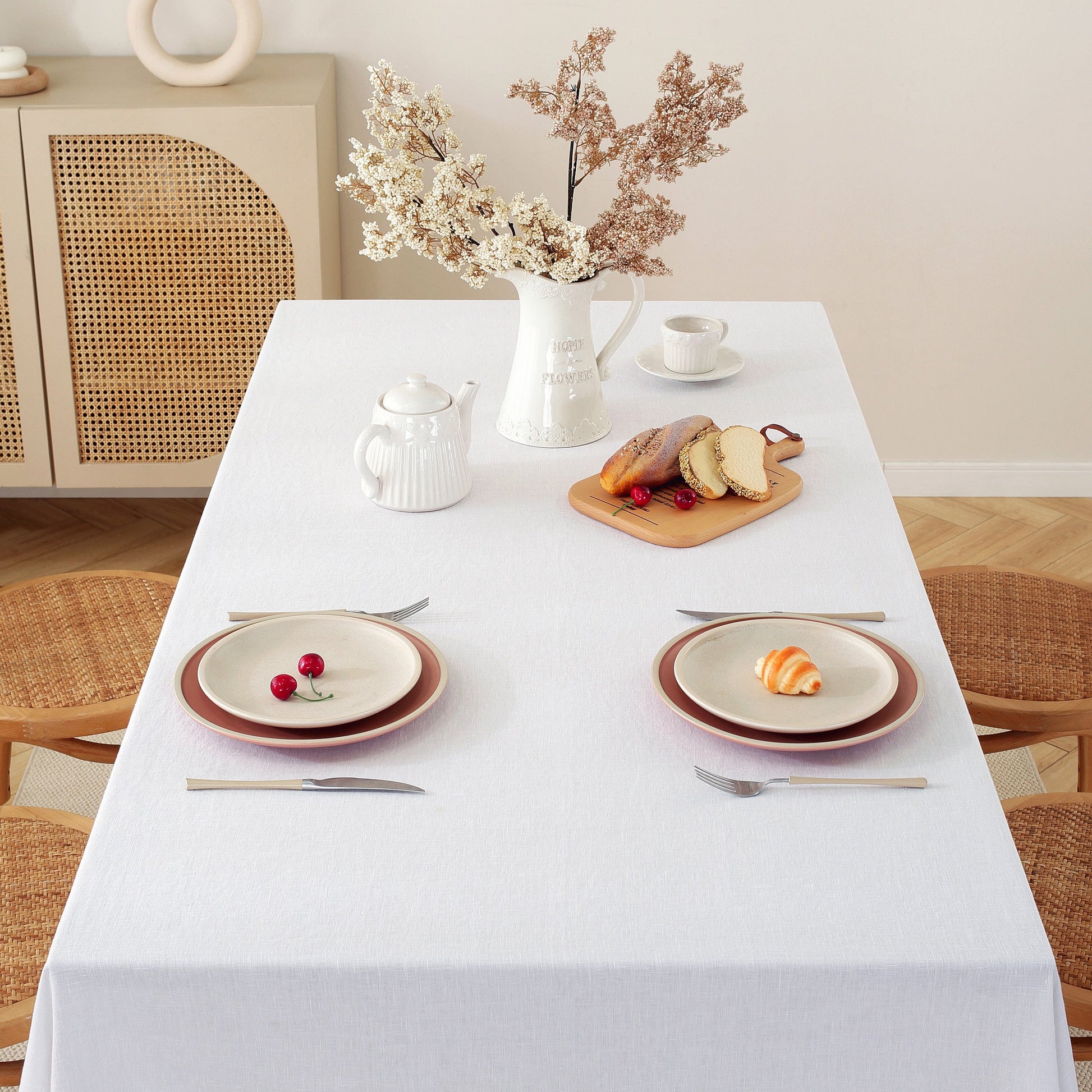 Dining table set with plates, cutlery, and a small arrangement of bread and fruit.
