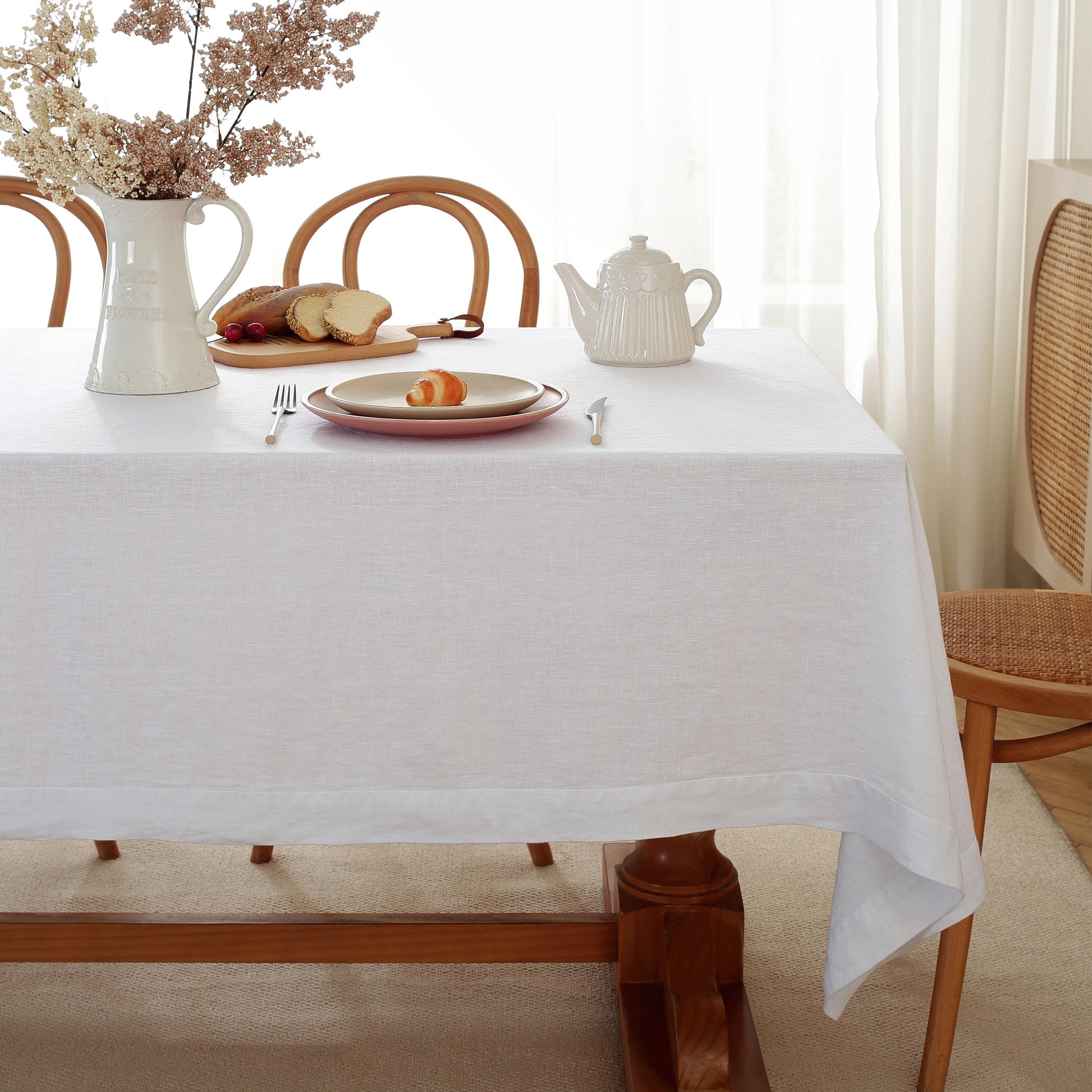 Dining table set with a white tablecloth, plates, teapot, and bread.