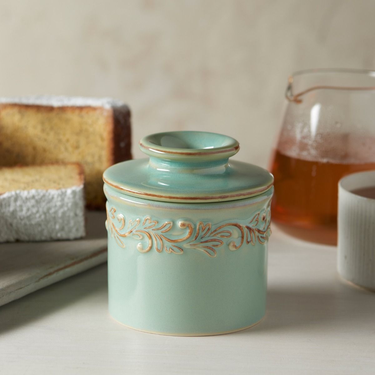 Decorative turquoise ceramic jar with intricate gold patterns on a table with bread and a glass of tea.