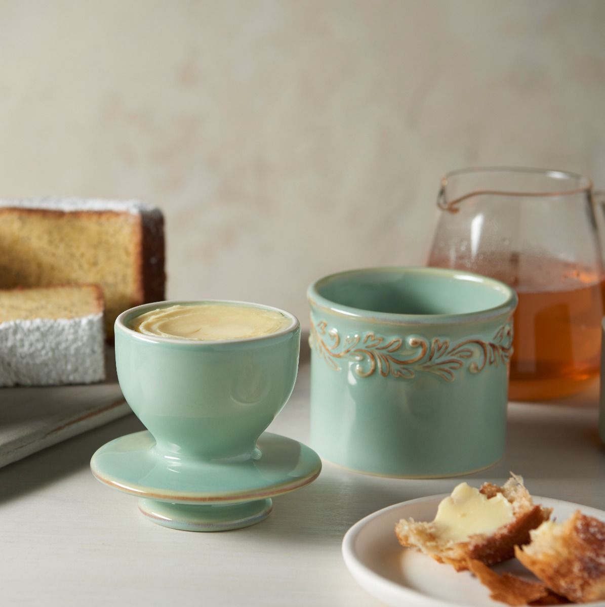 Two green ceramic cups with decorative patterns on a table with pastries and a glass of juice.