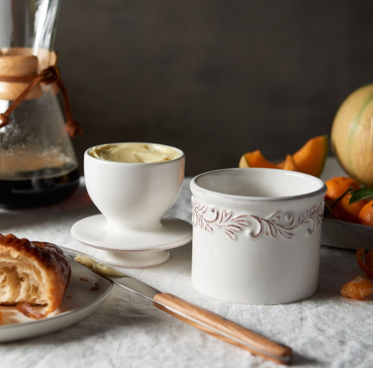 Ceramic cups with decorative patterns on a table with a croissant and coffee pot.