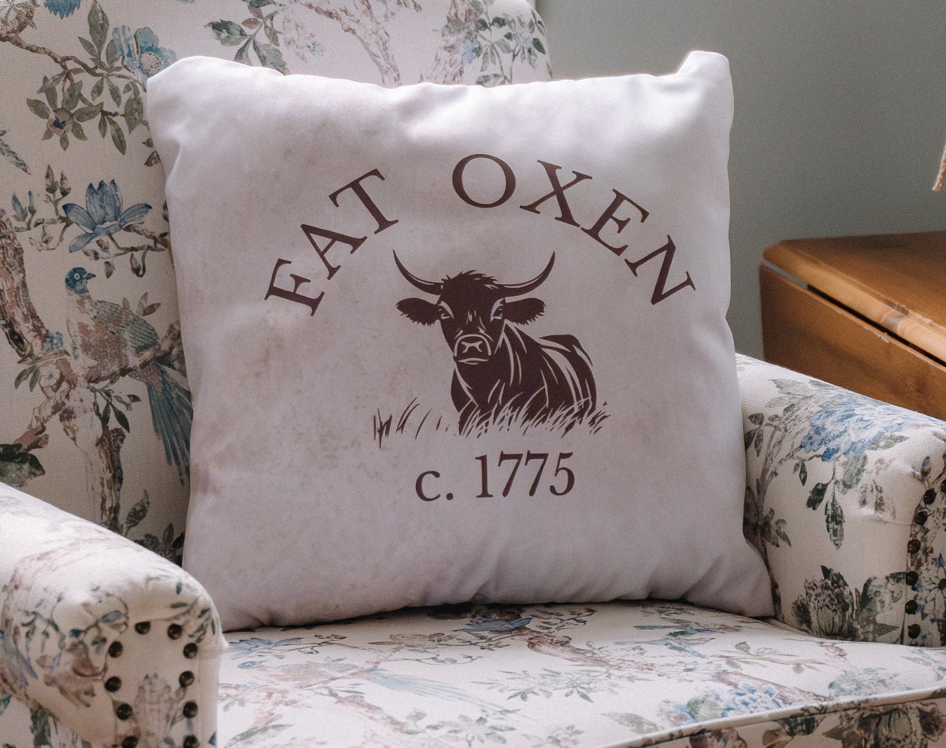 Decorative pillow with 'Fat Oxen' design on a floral armchair