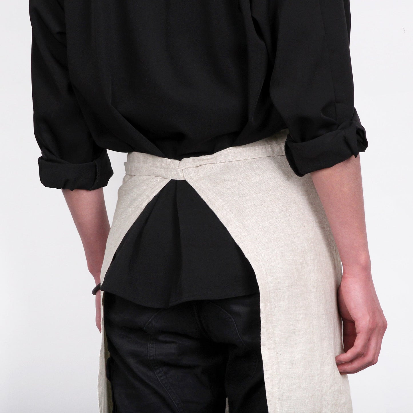 Person wearing a black shirt and a two-tone apron with black and beige sections on a white background