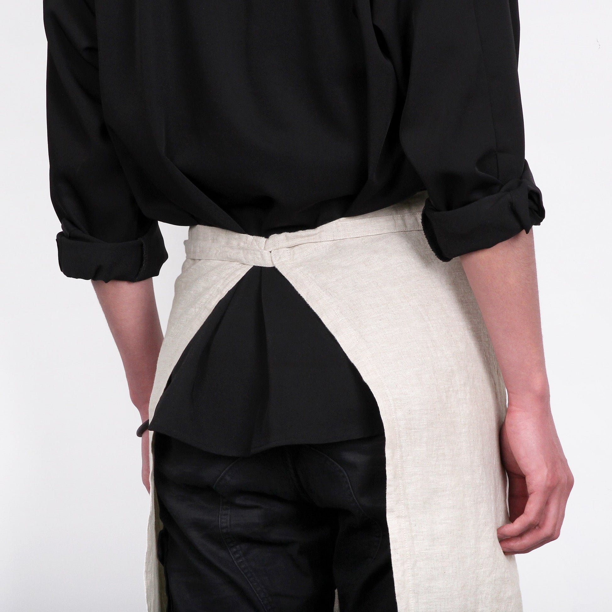 Person wearing a black shirt and a two-tone apron with black and beige sections on a white background