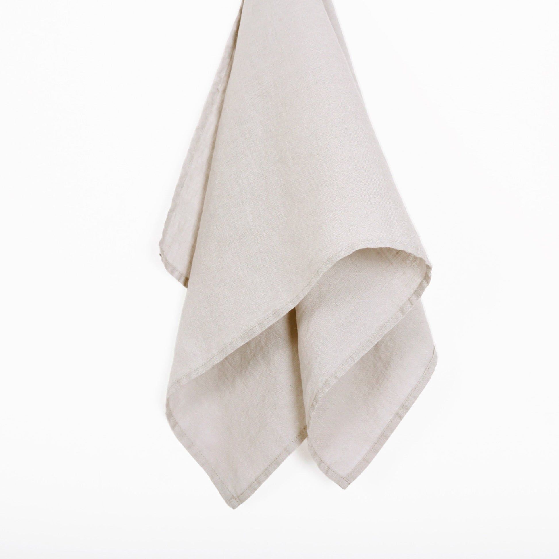 A light beige linen  tea towel, folded and hanging against a solid white background.