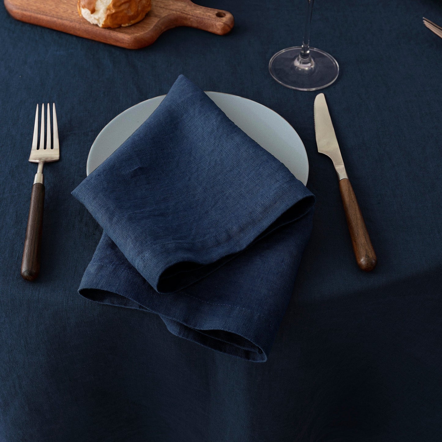 Navy blue napkin on a white plate with cutlery on a dark blue tablecloth