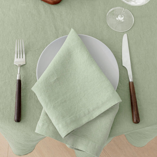 Green table setting with a folded napkin on a white plate, fork, knife, and wine glass on a green tablecloth.