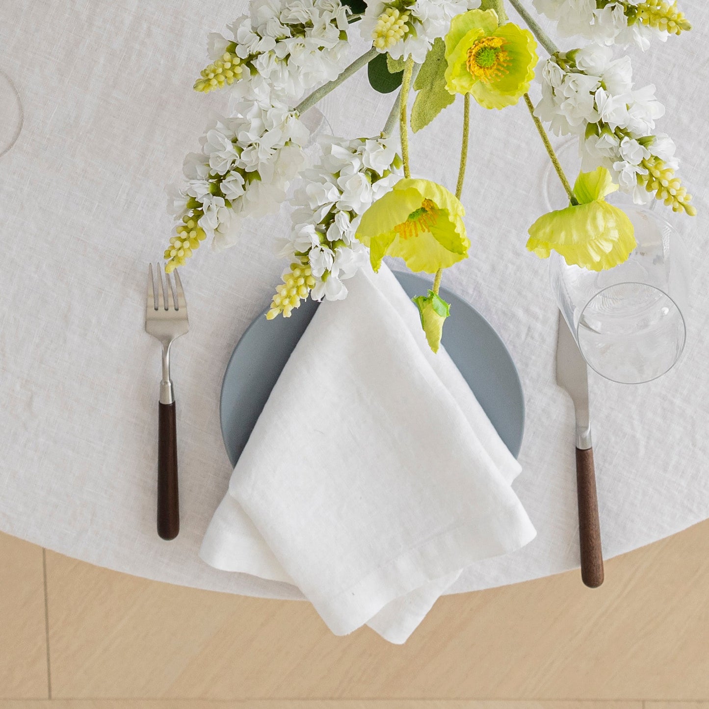 Dinner setting with a white napkin, gray plate, and floral decoration on a textured surface.