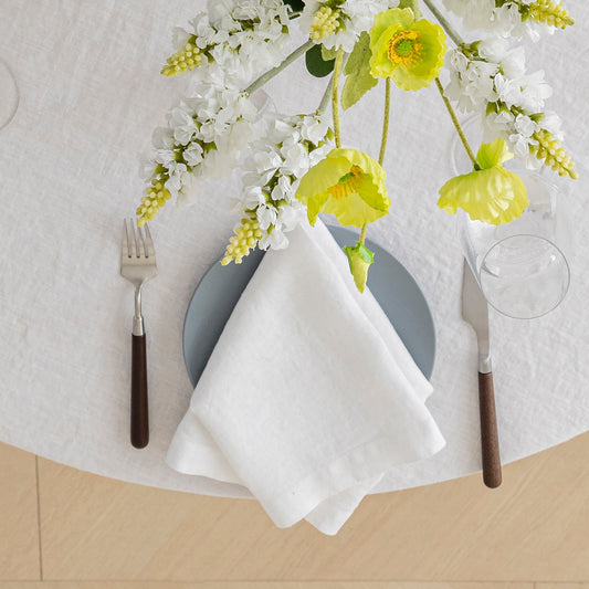 Dinner setting with a white napkin, gray plate, and floral decoration on a textured surface.