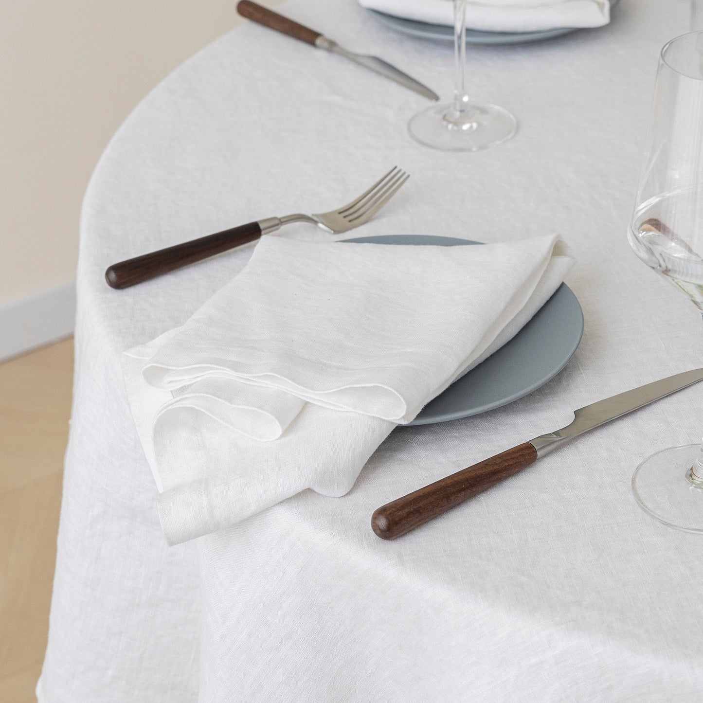 Table setting with white napkin, gray plate, and cutlery on a white tablecloth.