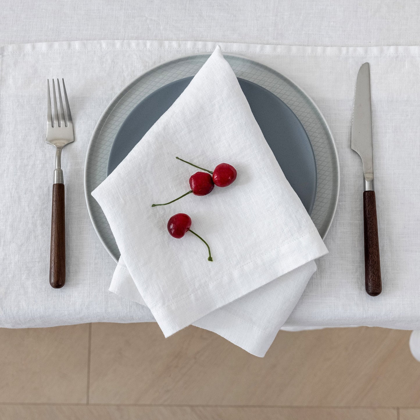 Table setting with a plate, napkin, and cherries on a white tablecloth.