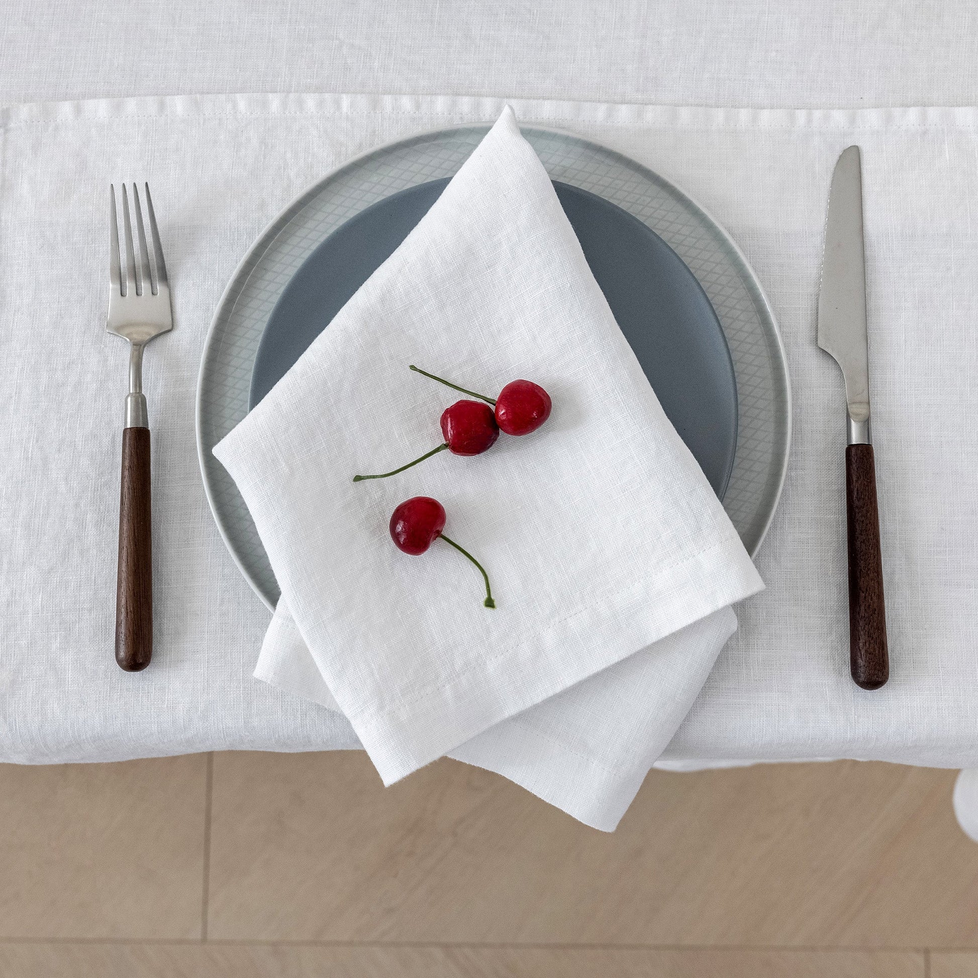 Table setting with a plate, napkin, and cherries on a white tablecloth.