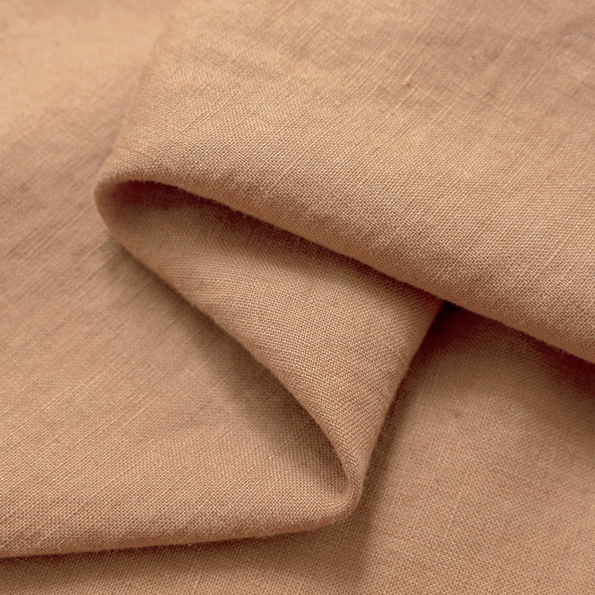 A close-up of draped fabric in a warm dusty tan or blush-beige color, showing the woven texture and soft folds.