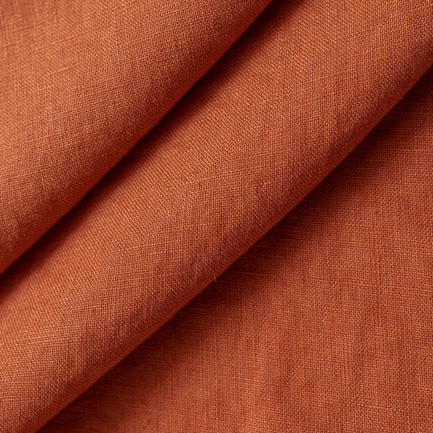 A close-up of draped rust-colored fabric with a visible woven texture, folded diagonally across the frame.