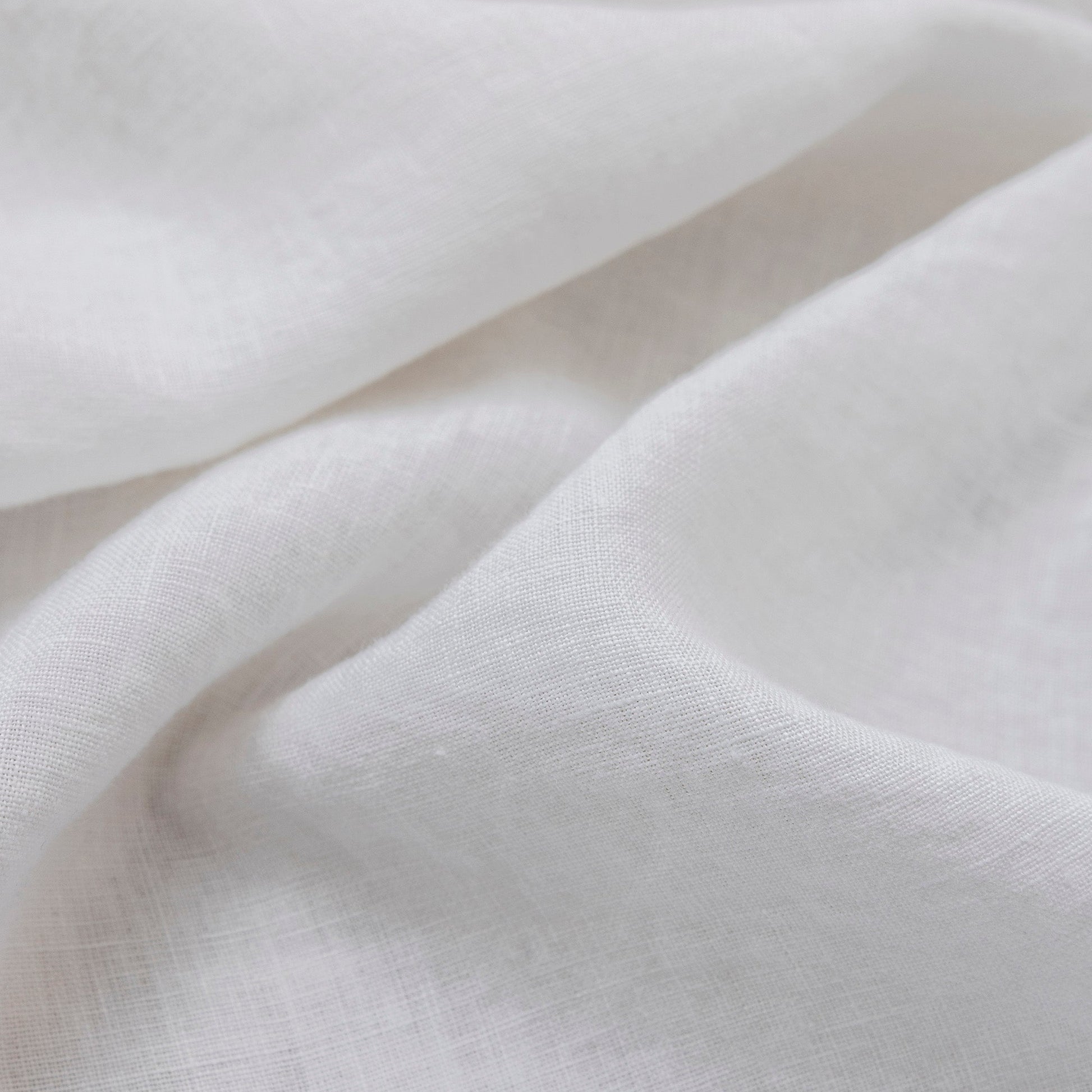 A close-up of draped white fabric with a soft, slightly textured weave and gentle folds.