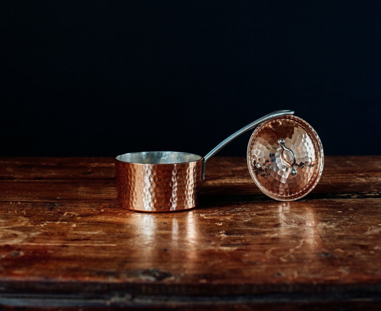 Copper saucepan butter pot with an open lid on a wooden surface