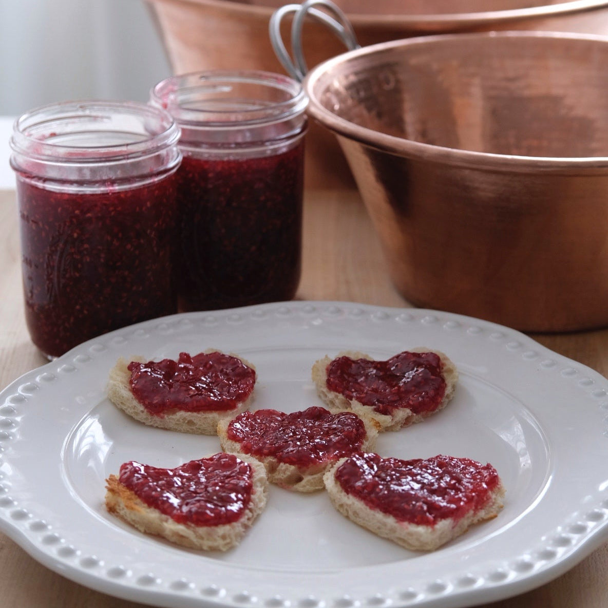 Jelly on bread slices with jars of jelly and a copper pot in the background.